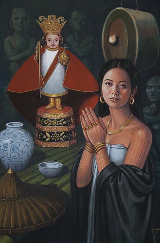 Queen Humamay, in precolonial Visayan attire, tattooos on her arms, gold around her neck and arms, prays in front of the Santo Nino image.