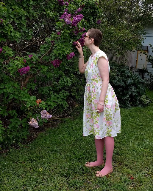 A woman poses in a garden, wearing a 50s style frock in a floral print
