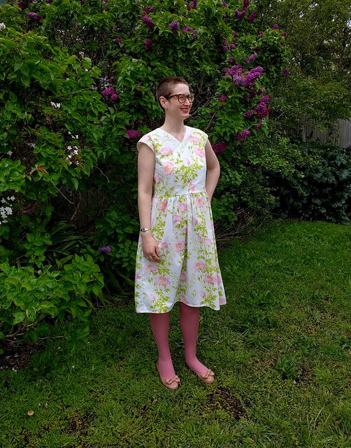 A woman poses in a garden, wearing a 50s style frock in a floral print