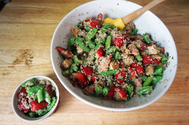 Strawberry-snap pea salad with quinoa and tofu, the large white bowl of it sitting on a wooden counter next to a small, bright red ramekin with a small portion of salad doled out.