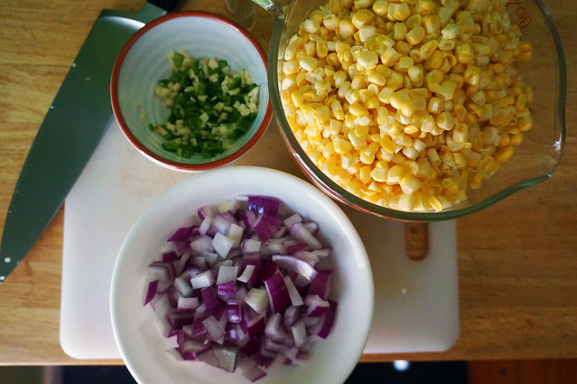 In bowls of various sizes, bright yellow corn, deep purple onion, and vibrant green jalapeño. This dish isn't Mardi Gras, but its colors are.