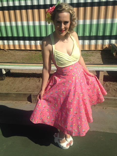 A woman wears a 50s-inspired shelf bust dress with matching floral headpiece.