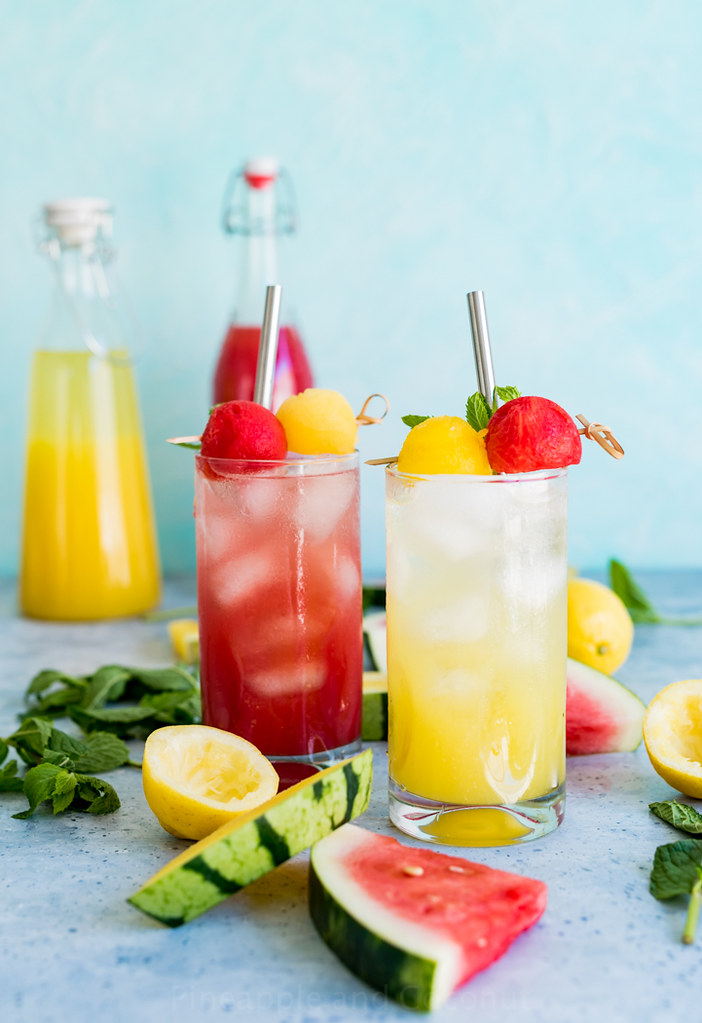 glasses of red watermelon lemonade and yellow watermelon lemonade with slices of watermelon lemons and mint
