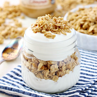 Granola in a glass jar with whipped cream and a spoon.